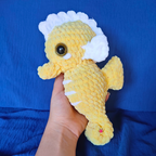 Yellow plush seahorse toy held against a blue background