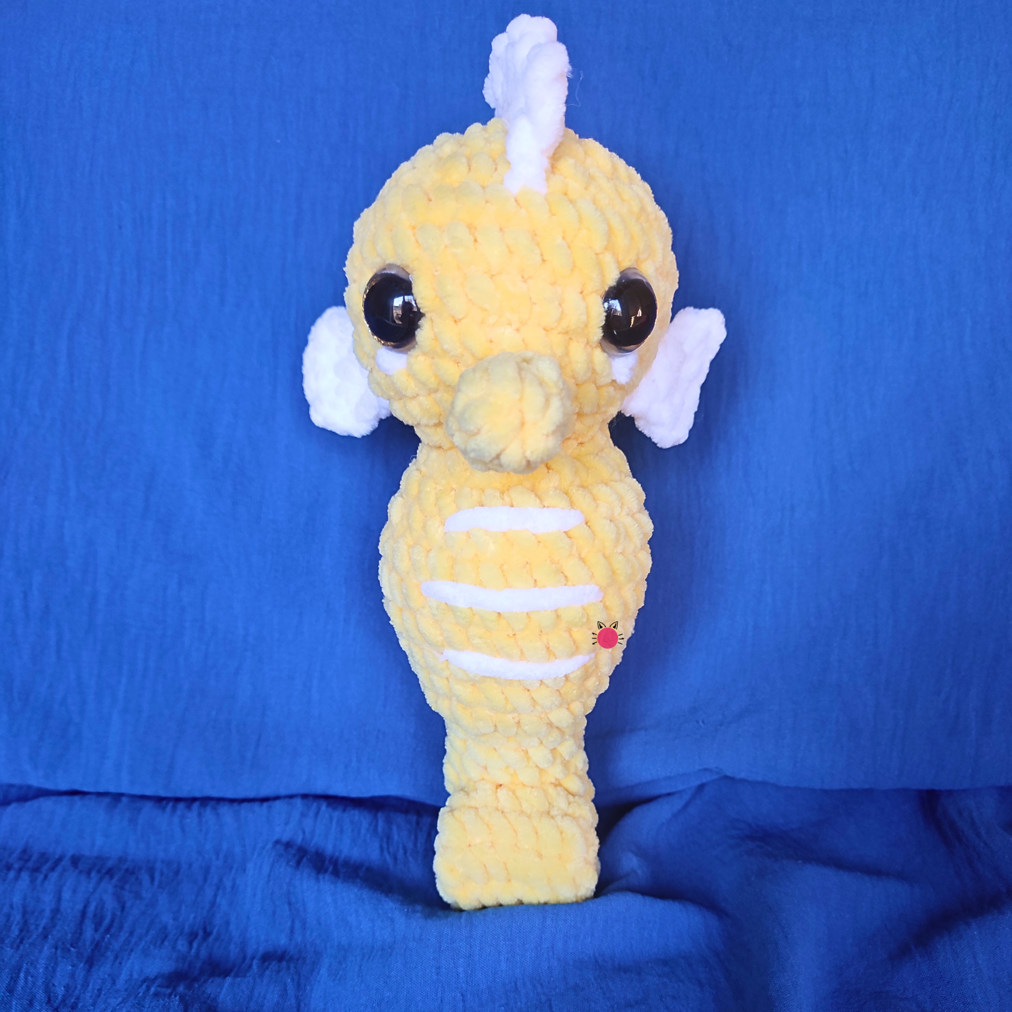 Yellow crochet plush toy with a white horn on a blue background